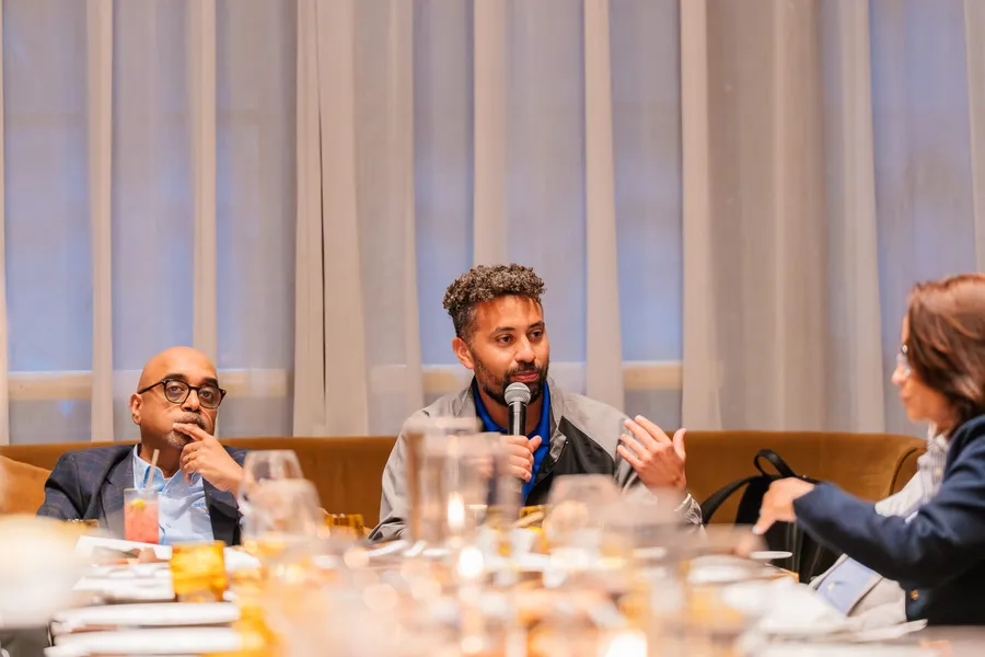 Panelist speaks into a microphone as a fellow panelist listens during an American Express dinner at Bourbon Steak