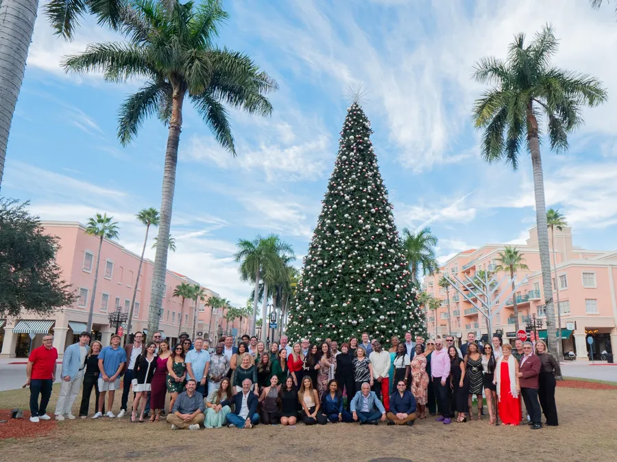 GED Lawyers team group photo under a giant Christmas tree and palm trees at their holiday celebration