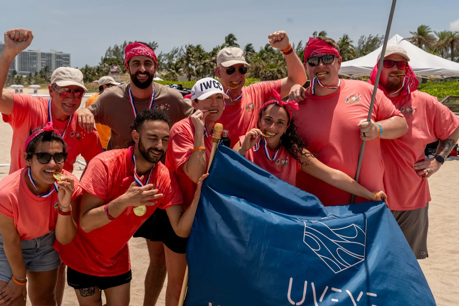 UVeye Beach Olympics winners biting gold medals behind a UVeye flag on Fort Lauderdale beach