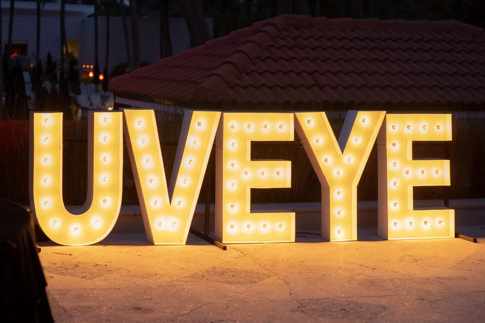 Giant illuminated UVEYE marquee letters glowing at dusk at the company anniversary party