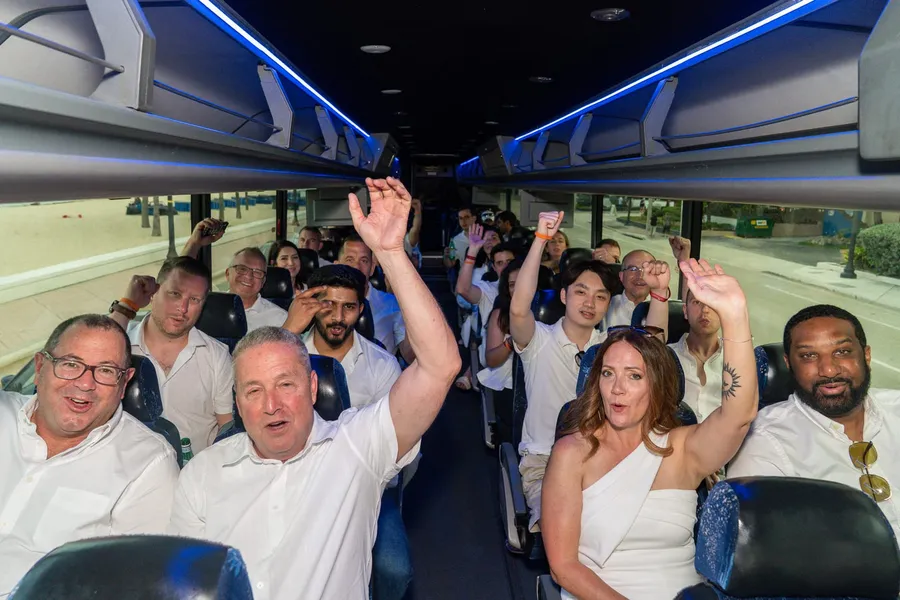 UVeye guests in white cheering with hands raised aboard a party bus lit with blue LED trim