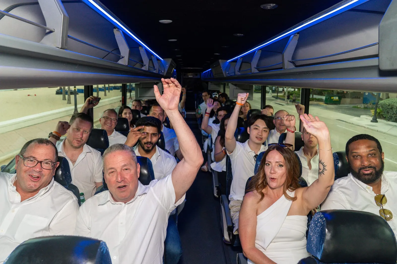 UVeye guests in white cheering with hands raised aboard a party bus lit with blue LED trim