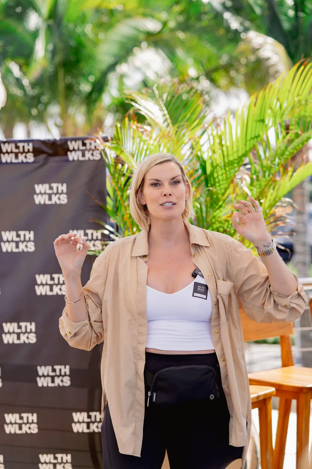 WLTH Walks host speaking to the group in front of a branded backdrop, palms behind her